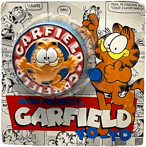 A blue and red yo-yo in original plastic and cardboard packaging. The toy is blue and red with a smiling 3D Garfield in the center. The packaging shows Garfield playing with a yo-yo and assorted black and white comic panels as the background.